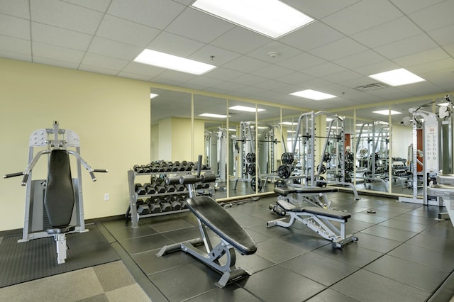 gym featuring a paneled ceiling and baseboards