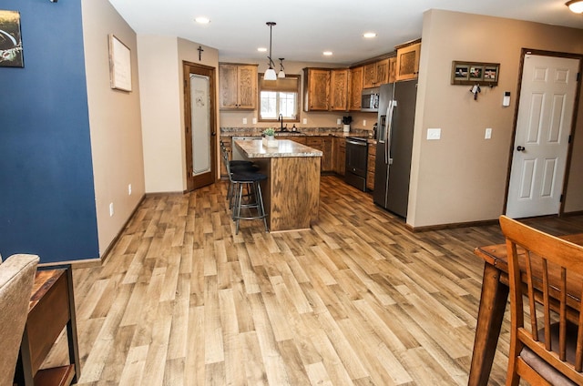 kitchen with a kitchen island, appliances with stainless steel finishes, decorative light fixtures, light stone counters, and light hardwood / wood-style floors