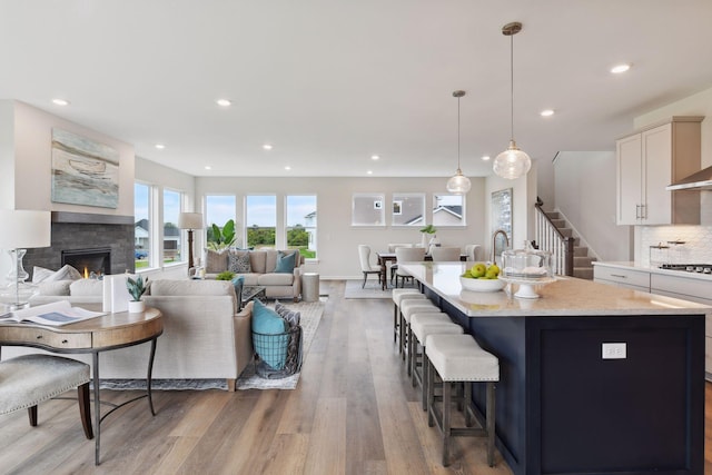 kitchen with light hardwood / wood-style flooring, gas cooktop, a kitchen island with sink, white cabinetry, and decorative light fixtures