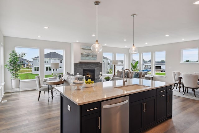 kitchen with sink, light hardwood / wood-style flooring, dishwasher, a kitchen island with sink, and decorative light fixtures