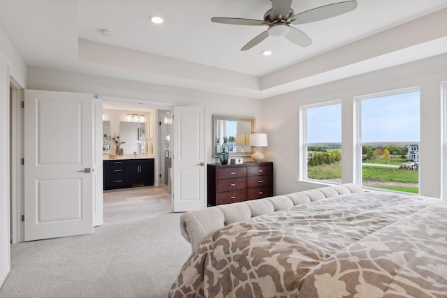 carpeted bedroom featuring a raised ceiling, ceiling fan, and ensuite bath