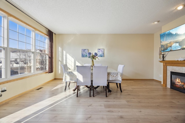 dining space featuring light hardwood / wood-style flooring, a high end fireplace, and a textured ceiling