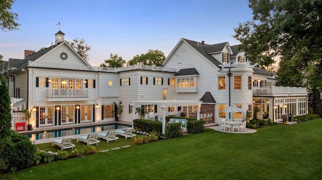 20100 Lakeview Ave, Deephaven, MN 55331 - back of house at dusk with a pergola, an outdoor pool, a lawn, and a balcony