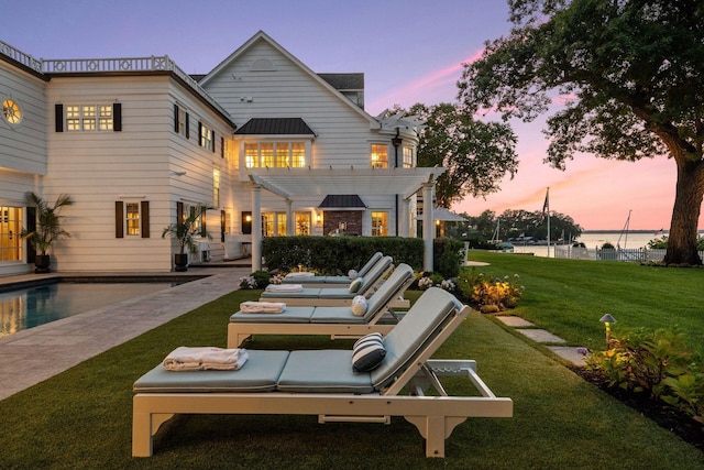 20100 Lakeview Ave, Deephaven, MN 55331 - back of property at dusk featuring a pergola, a standing seam roof, a lawn, a metal roof, and an outdoor pool