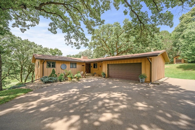 ranch-style home featuring driveway, an attached garage, board and batten siding, and a chimney