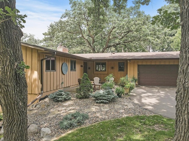 view of front of property featuring driveway, a chimney, an attached garage, and board and batten siding