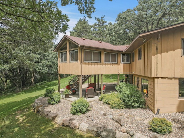 rear view of house featuring a patio area, a shingled roof, stairs, and a yard