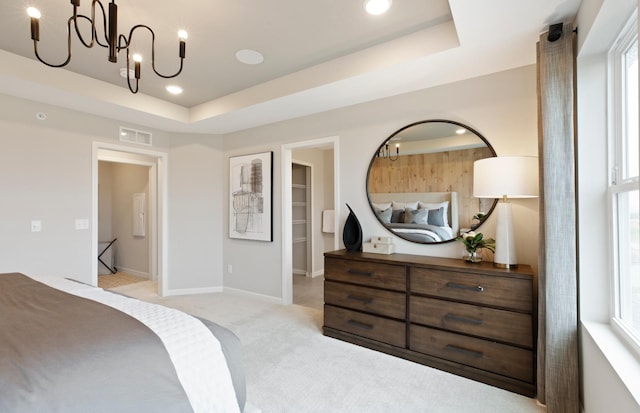 bedroom featuring multiple windows, a walk in closet, light colored carpet, a notable chandelier, and a tray ceiling