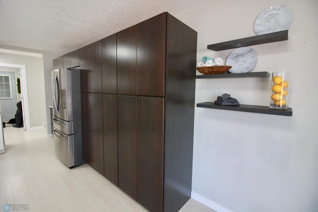 kitchen with dark brown cabinets, a textured ceiling, stainless steel refrigerator, and light hardwood / wood-style flooring