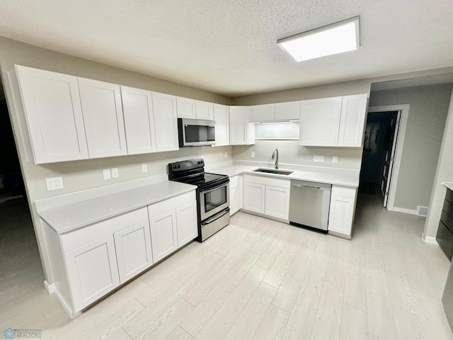 kitchen with sink, white cabinets, stainless steel appliances, a textured ceiling, and light hardwood / wood-style flooring