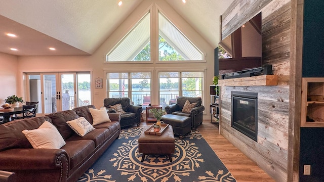 living room featuring high vaulted ceiling, a fireplace, light hardwood / wood-style floors, and french doors