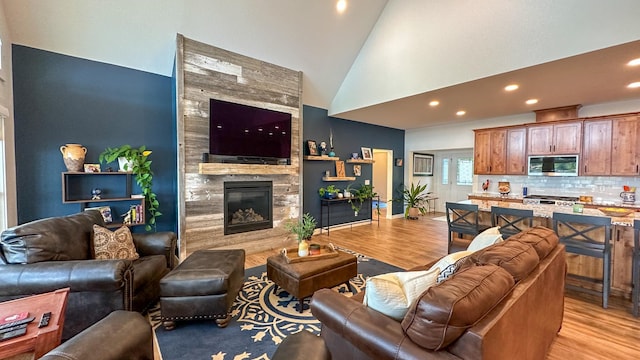 living room with high vaulted ceiling, a fireplace, and light hardwood / wood-style floors