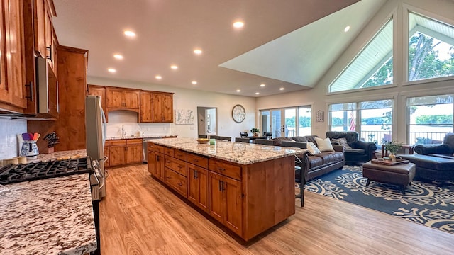 kitchen featuring light hardwood / wood-style flooring, a kitchen breakfast bar, stainless steel appliances, light stone countertops, and an island with sink