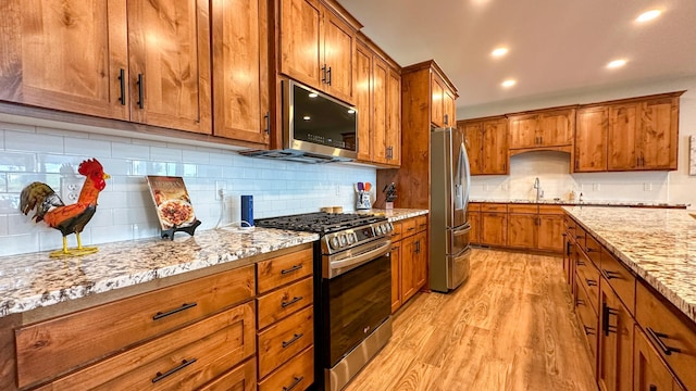 kitchen featuring sink, light wood-type flooring, stainless steel appliances, light stone countertops, and backsplash