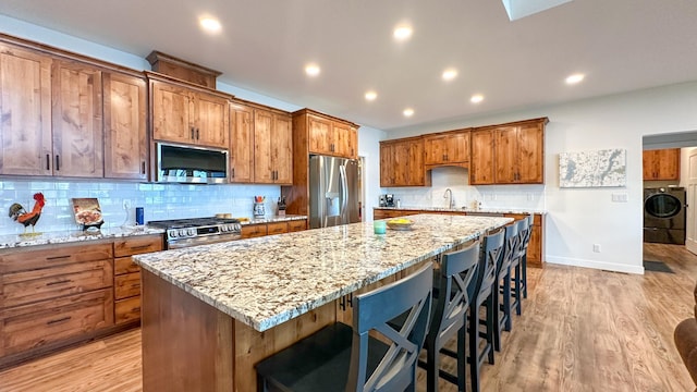 kitchen with a kitchen island, stainless steel appliances, light stone countertops, a kitchen bar, and washer / clothes dryer