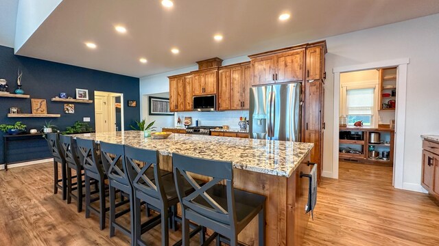 kitchen featuring a breakfast bar, light stone counters, stainless steel appliances, a large island, and light hardwood / wood-style floors