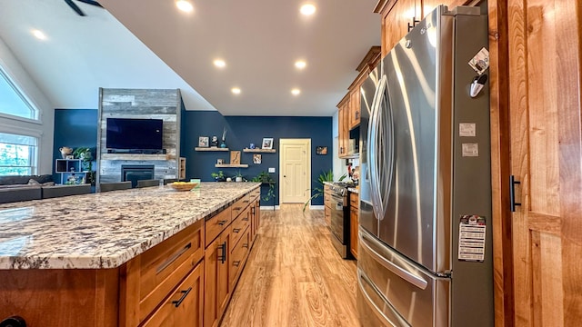 kitchen featuring a tile fireplace, lofted ceiling, light stone counters, stainless steel appliances, and light wood-type flooring