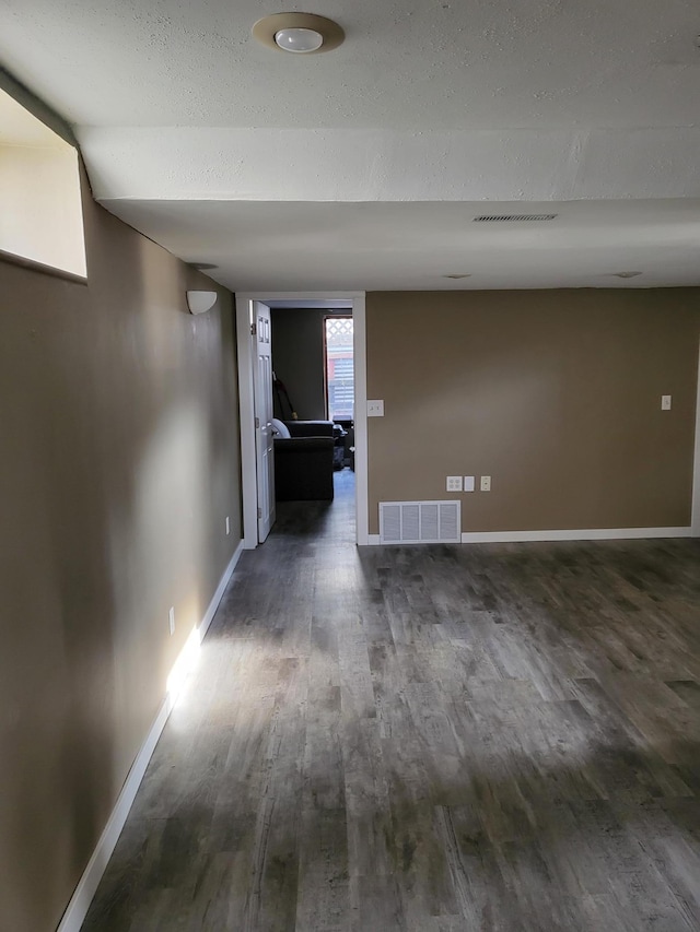 hallway with dark wood-type flooring, baseboards, visible vents, and a textured ceiling