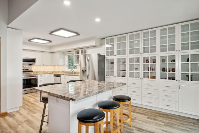 kitchen with sink, stainless steel appliances, a center island, white cabinets, and a kitchen bar