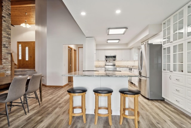 kitchen with a center island, appliances with stainless steel finishes, light stone countertops, decorative backsplash, and white cabinets