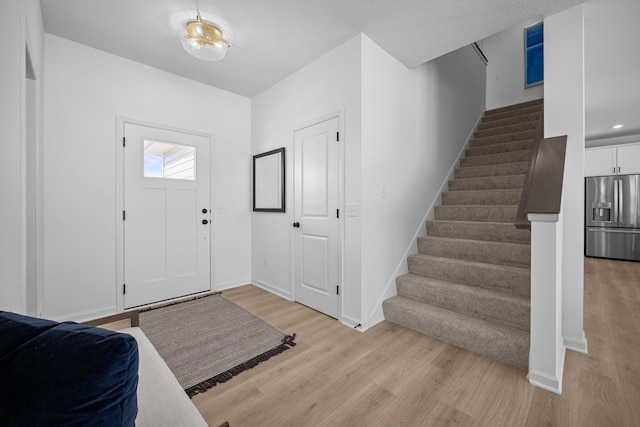 foyer entrance featuring light wood-style flooring, stairs, and baseboards