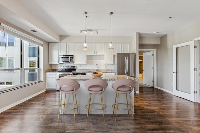 kitchen with a kitchen island, decorative light fixtures, white cabinets, stainless steel appliances, and light stone countertops