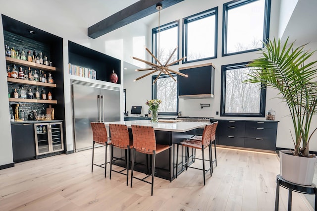 kitchen featuring light hardwood / wood-style flooring, stainless steel built in refrigerator, a healthy amount of sunlight, a kitchen bar, and beverage cooler