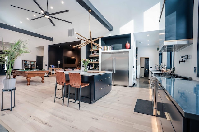 kitchen featuring stainless steel built in refrigerator, a kitchen bar, a center island, a towering ceiling, and wall chimney range hood