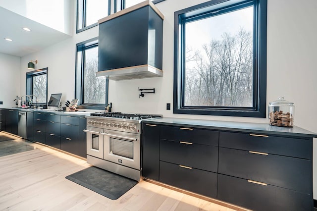 kitchen with a wealth of natural light, appliances with stainless steel finishes, wall chimney range hood, and light hardwood / wood-style floors