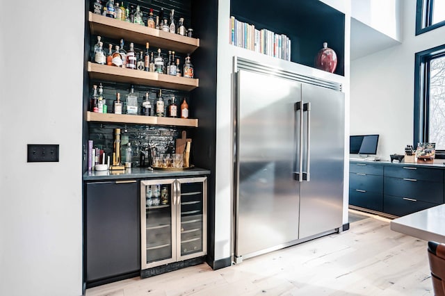 bar featuring built in refrigerator, beverage cooler, and light hardwood / wood-style floors