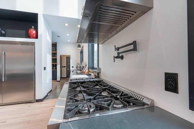 kitchen featuring wood-type flooring, stainless steel built in fridge, cooktop, and ventilation hood