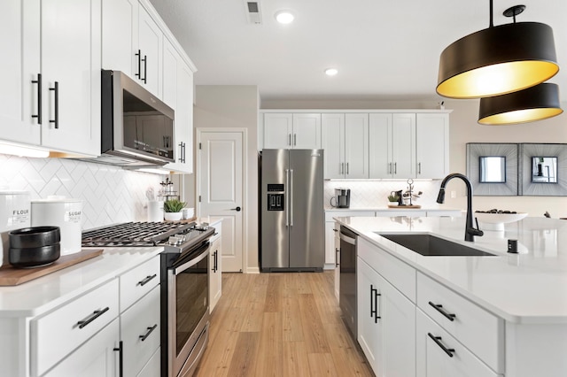 kitchen with appliances with stainless steel finishes, sink, white cabinets, hanging light fixtures, and light wood-type flooring