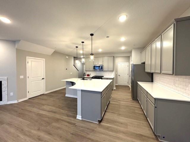 kitchen with sink, a center island with sink, hardwood / wood-style flooring, pendant lighting, and backsplash