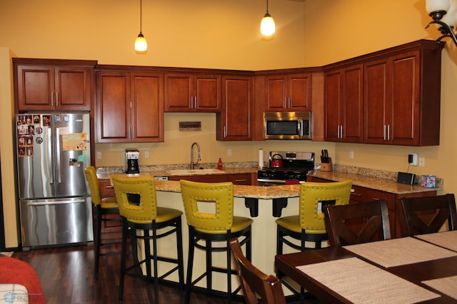 kitchen with light stone counters, stainless steel appliances, sink, and hanging light fixtures