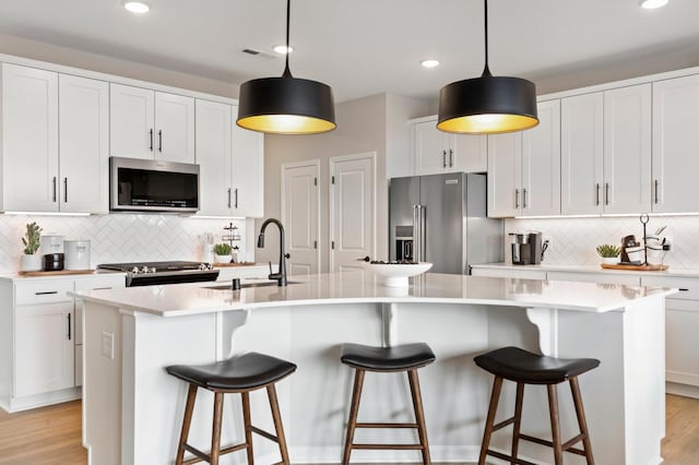 kitchen with a breakfast bar area, a center island with sink, pendant lighting, stainless steel appliances, and white cabinets