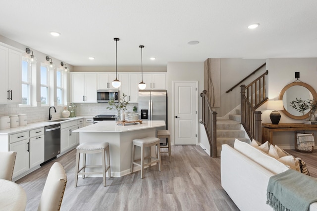 kitchen with decorative light fixtures, a kitchen island, white cabinets, and appliances with stainless steel finishes