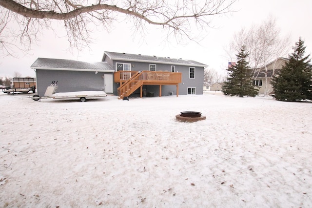 snow covered back of property with a wooden deck and a fire pit