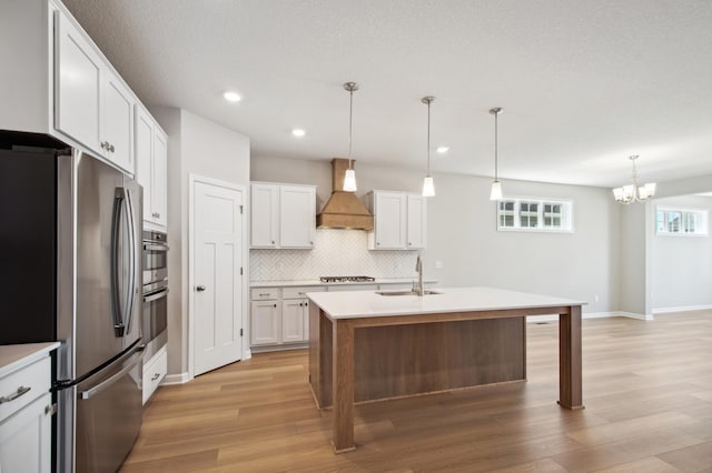 kitchen with a center island with sink, custom range hood, pendant lighting, stainless steel appliances, and white cabinets