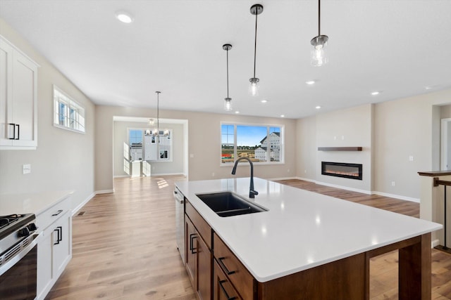 kitchen with an island with sink, light hardwood / wood-style floors, sink, and hanging light fixtures