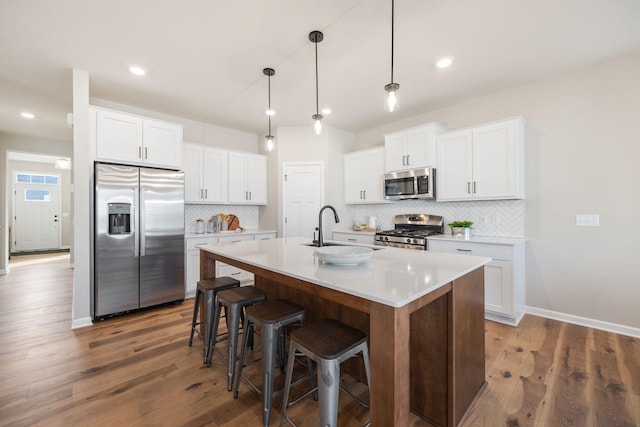 kitchen with sink, white cabinetry, decorative light fixtures, an island with sink, and stainless steel appliances