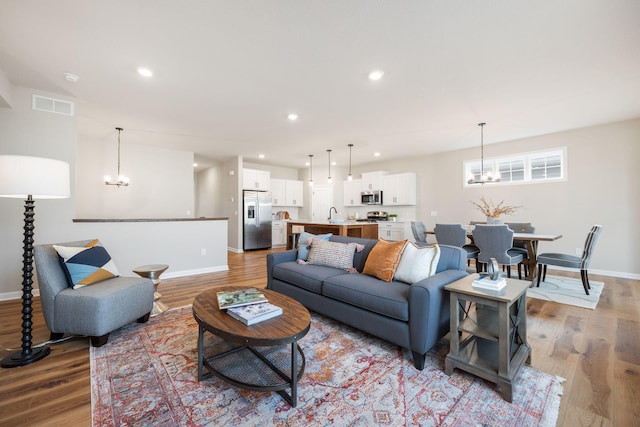 living room featuring an inviting chandelier, sink, and light hardwood / wood-style floors