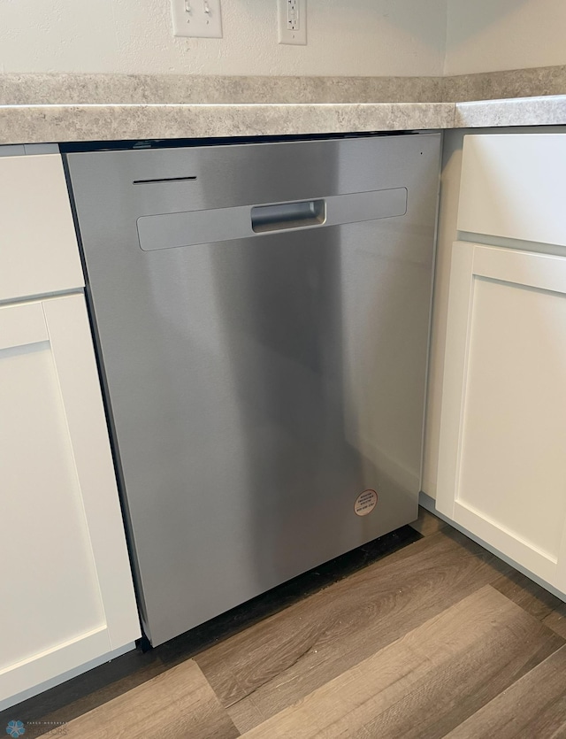 interior details with stainless steel dishwasher, white cabinets, and light wood-type flooring