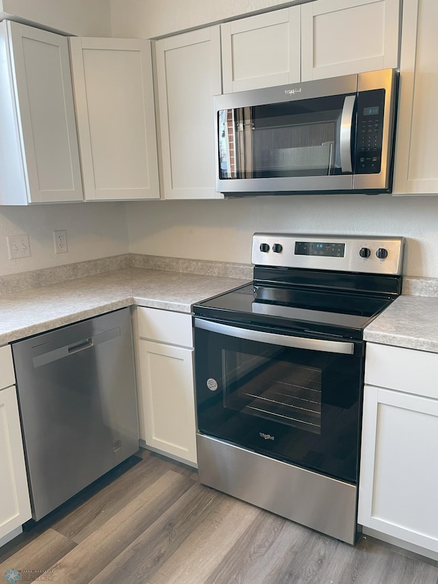 kitchen with stainless steel appliances, wood-type flooring, and white cabinets