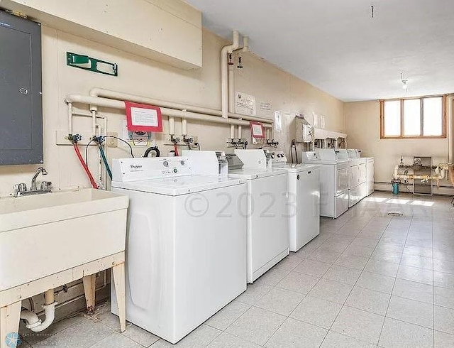 laundry room featuring light tile patterned flooring, washing machine and clothes dryer, electric panel, and sink