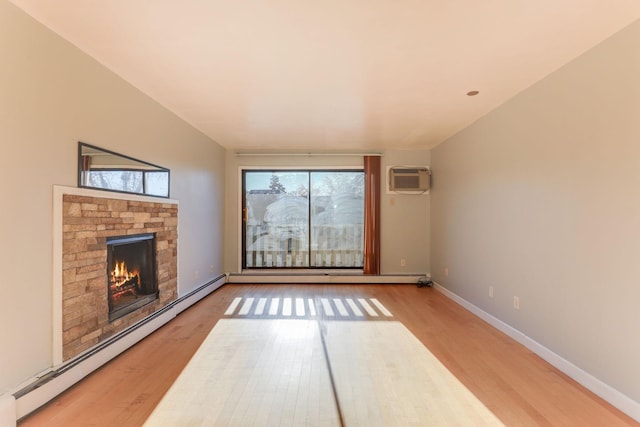 unfurnished living room with a wall mounted AC, a stone fireplace, hardwood / wood-style floors, and baseboard heating