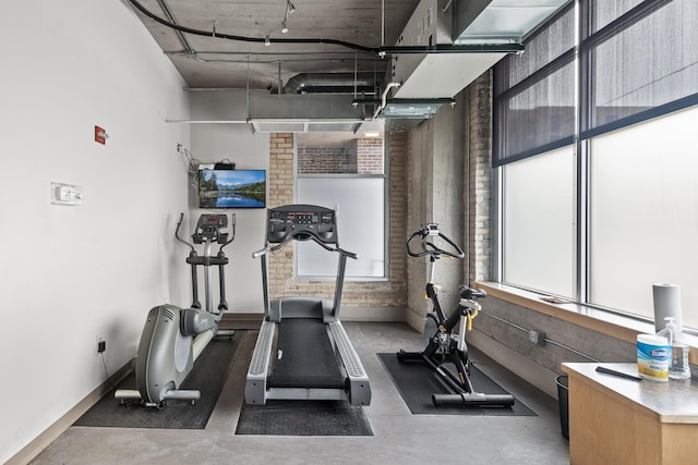 exercise area featuring brick wall, a healthy amount of sunlight, and track lighting