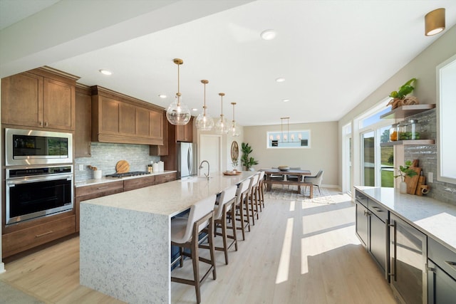 kitchen featuring pendant lighting, stainless steel appliances, light stone counters, decorative backsplash, and a large island with sink