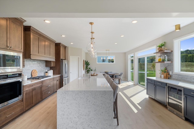 kitchen with a kitchen island, appliances with stainless steel finishes, wine cooler, hanging light fixtures, and light wood-type flooring