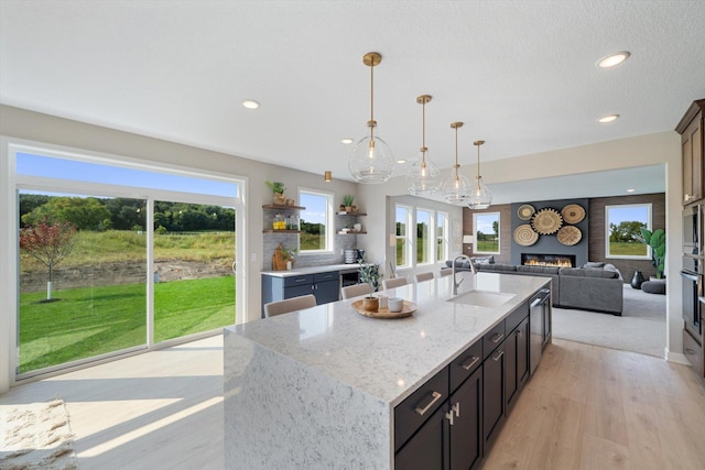 kitchen featuring pendant lighting, sink, light stone counters, stainless steel appliances, and a center island with sink