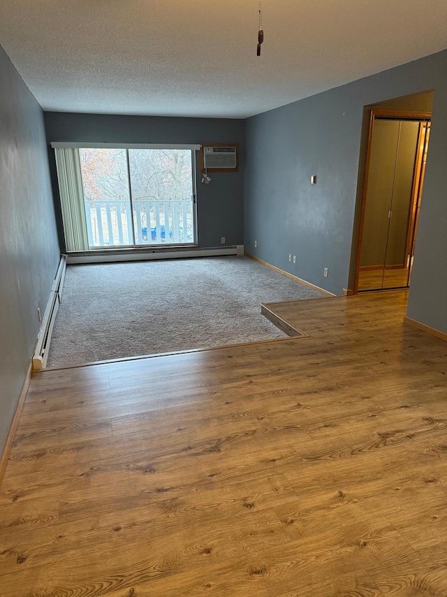 unfurnished room featuring a wall unit AC, a textured ceiling, light hardwood / wood-style flooring, and a baseboard heating unit